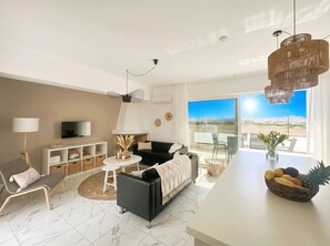 Un salon moderne avec un canapĂ©, un tĂ©lĂ©viseur et un coin repas agrĂ©mentĂ© dâun panier de fruits.