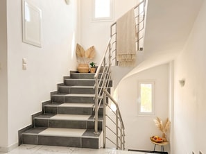 Eine Treppe mit Metallgeländer, einer Wandleuchte und einem kleinen Tisch mit einer Vase und Früchten.