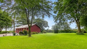 Um celeiro vermelho com um campo gramado e árvores ao fundo.