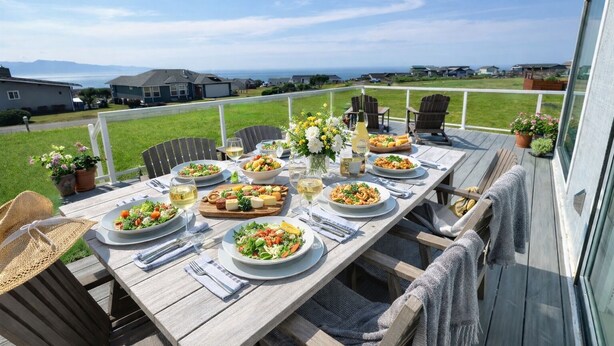 A wooden deck with a table set for a meal, outdoor chairs, and potted plants.
