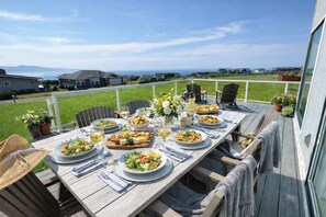 Eine Holzterrasse mit Esstisch, Gartenstühlen und Topfpflanzen.