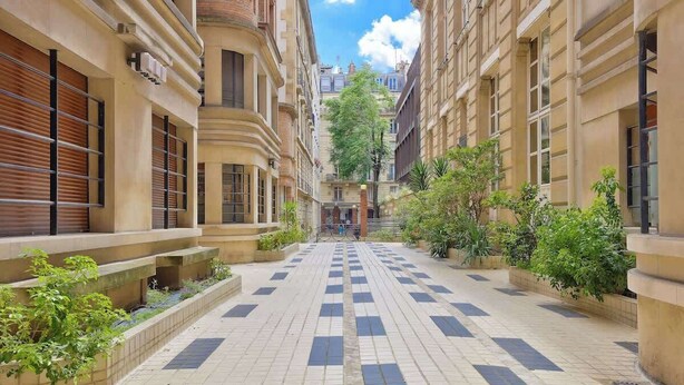 A narrow, tiled pedestrian walkway flanked by buildings with large windows and balconies, leading to a central entrance. - Splendid Apartment in the Heart of the Chic 16th (Paris)