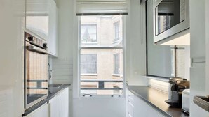 A narrow kitchen with white cabinets, a black countertop, and a window with a view of buildings. - Splendid Apartment in the Heart of the Chic 16th (Paris)