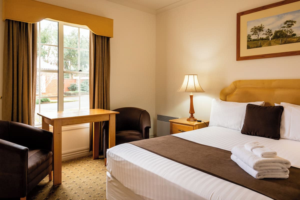 A hotel room with a bed, a desk, a chair, a lamp, and a painting on the wall.