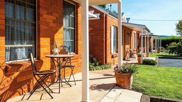 A brick building with a covered patio area, outdoor seating, and a well-maintained lawn. - Riverview at Ross (Ross)