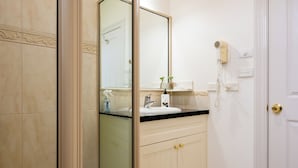 A bathroom with a glass shower enclosure, a sink with a mirror, and a hairdryer mounted on the wall. - Riverview at Ross (Ross)