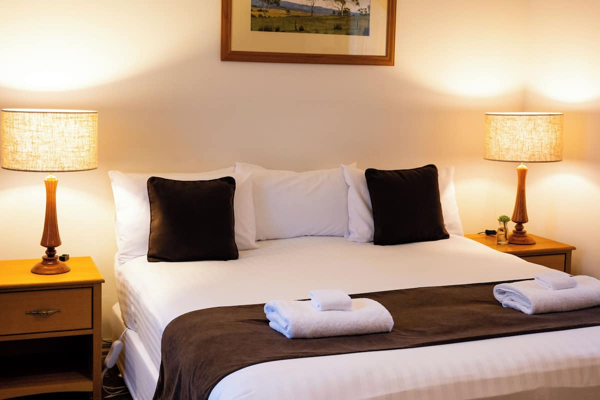 A neatly made bed with white and dark pillows, two bedside lamps, and folded towels on the bed.