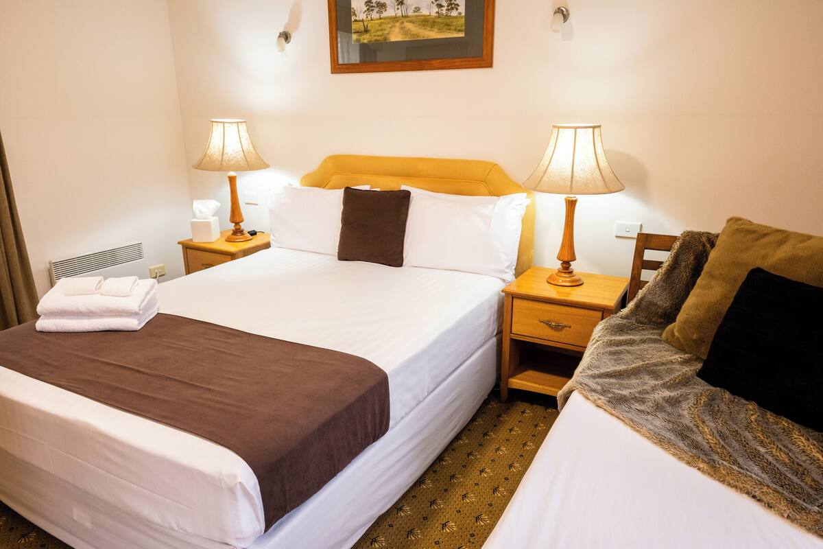 A hotel room with a large bed, two bedside tables with lamps, a nightstand, and a small table with a lamp.