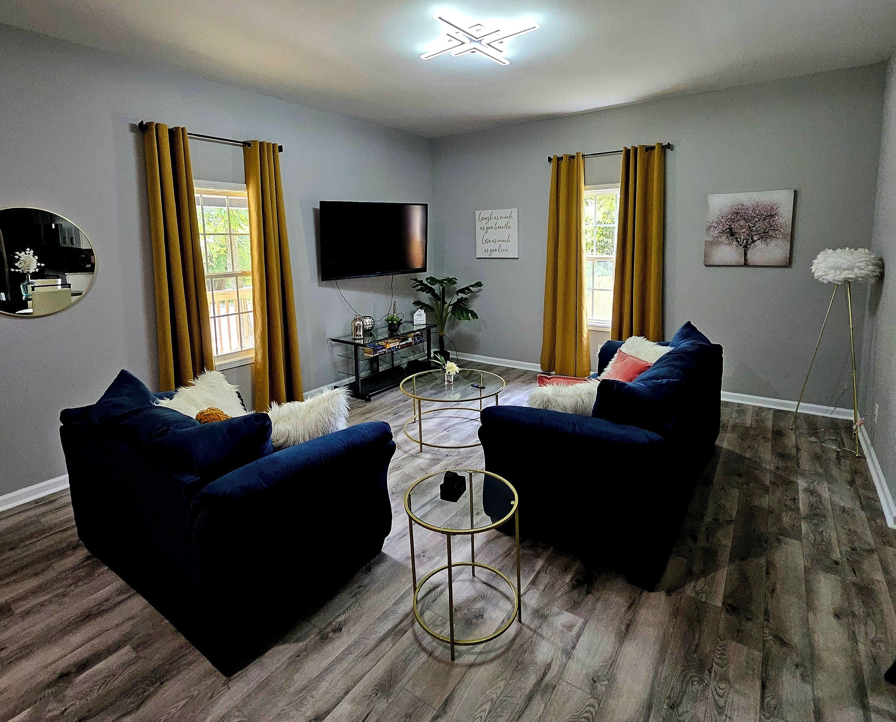 A living room with two blue armchairs, a glass coffee table, a flat-screen TV, and a bookshelf.