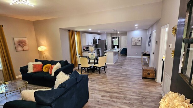 A modern living room with dark blue sofas, a glass coffee table, and a dining area with yellow chairs.