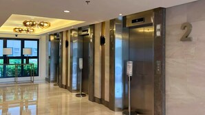 A modern elevator area with a polished floor, a chandelier, and a large window with a view. - Acellyne's Suites at Green 2 Residences (Dasmarinas)