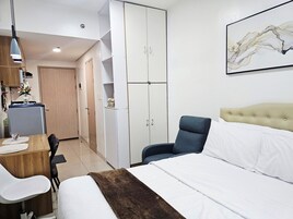 Habitación de hotel con cama, escritorio con silla, armario y un cuadro en la pared.