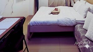 A hotel room with a bed, a desk, a chair, a TV, an air conditioning unit, and a ceiling light fixture. - Acellyne's Suites at Green 2 Residences (Dasmarinas)