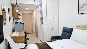 Un dormitorio con cama, escritorio, silla, armario y kitchenette.