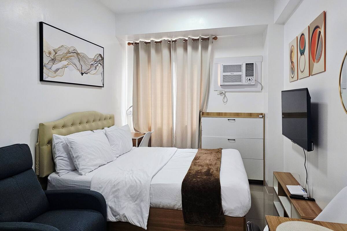 A hotel room with a bed, a desk, a chair, a TV, and artwork on the walls.