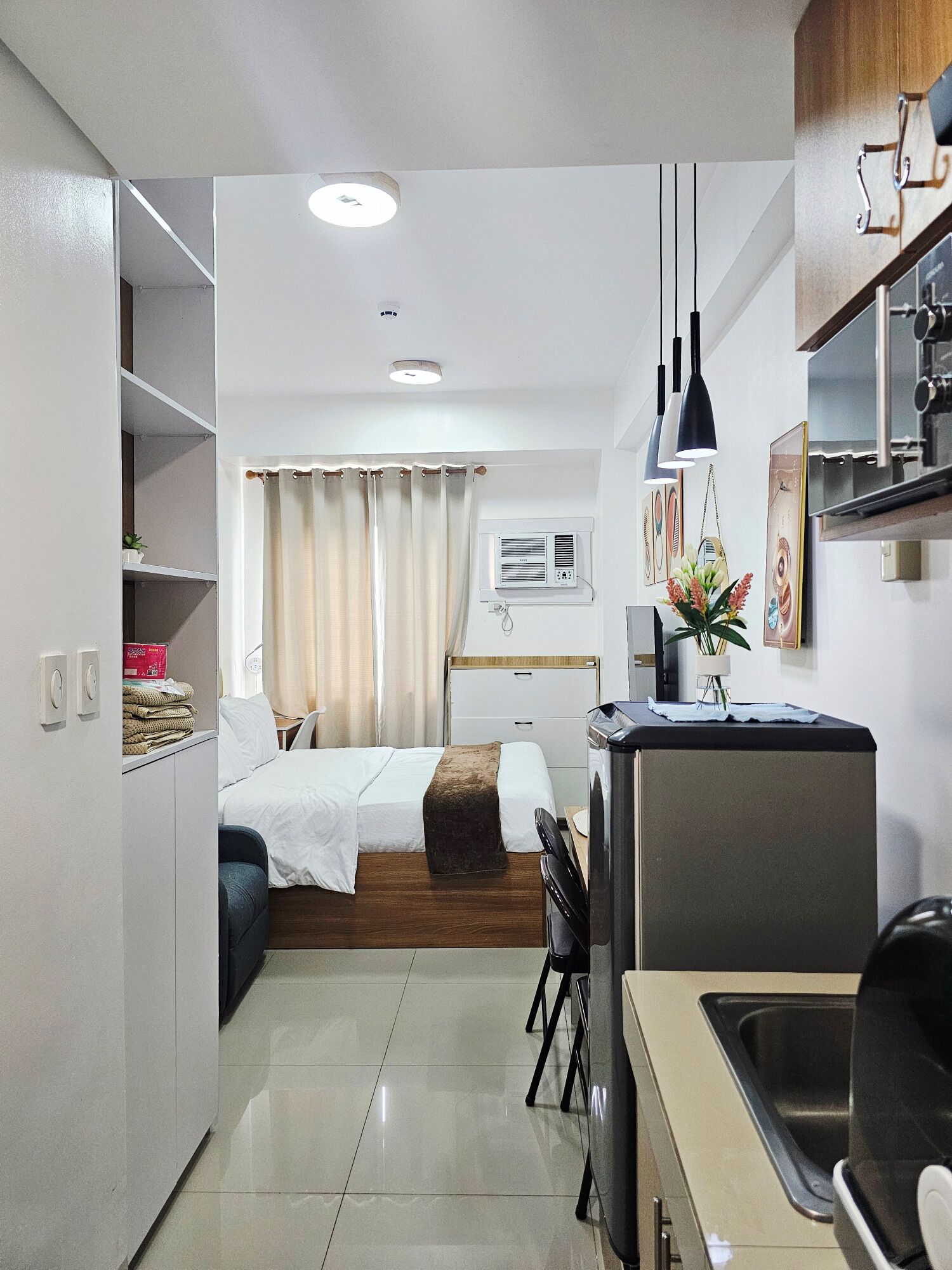 Quarto de hotel compacto com cama, pequena cozinha, área de refeições e banheiro.