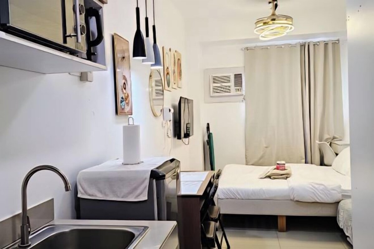 Una habitación de hotel compacta con kitchenette, cama, escritorio y zona de ducha.