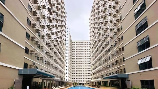 A swimming pool with lounge chairs in the foreground, surrounded by high-rise residential buildings. - Acellyne's Suites at Green 2 Residences (Dasmarinas)