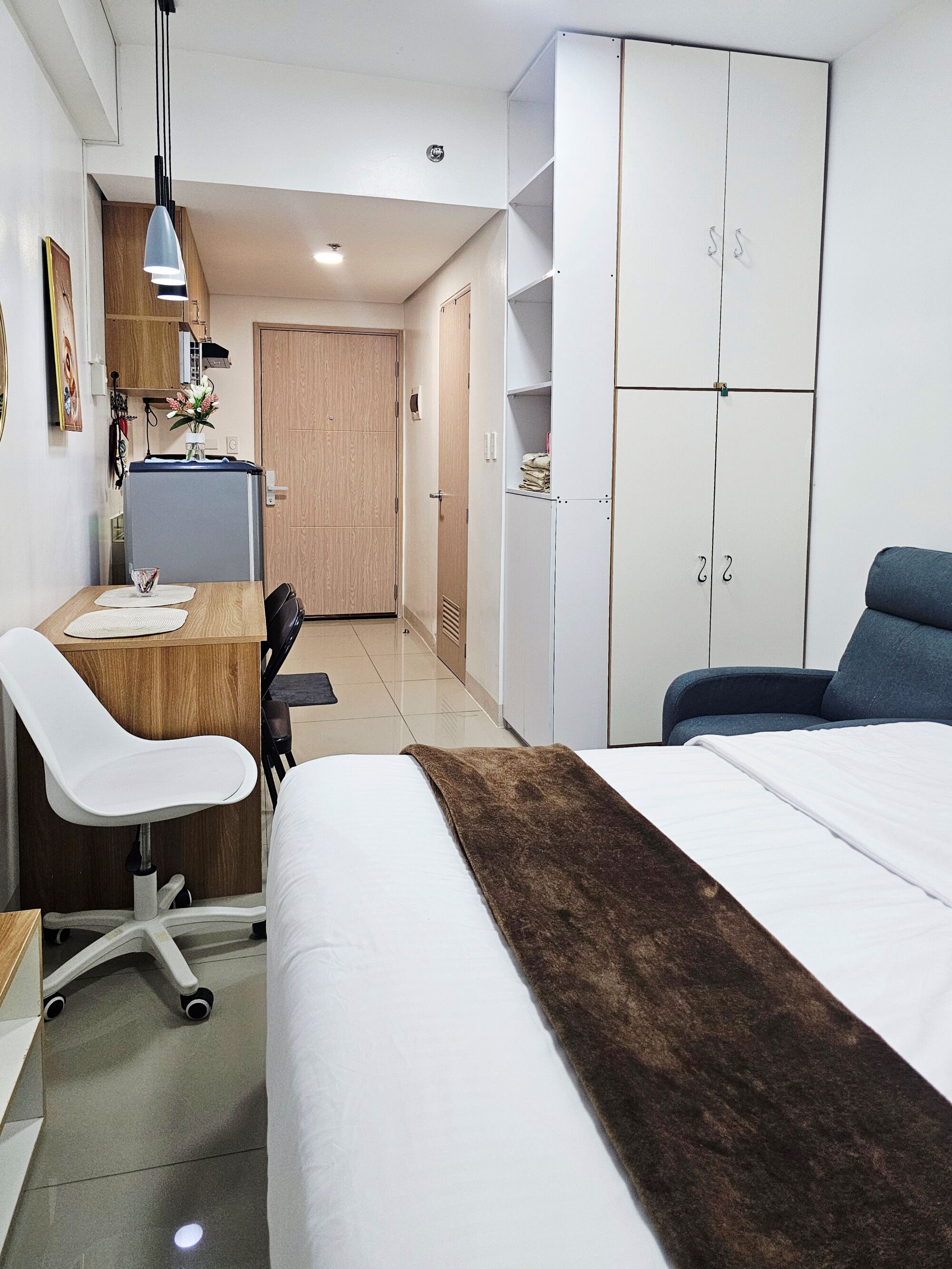Habitación de hotel con cama, escritorio con silla, armario y kitchenette.