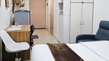 Habitación de hotel con cama, escritorio con silla, armario y kitchenette.