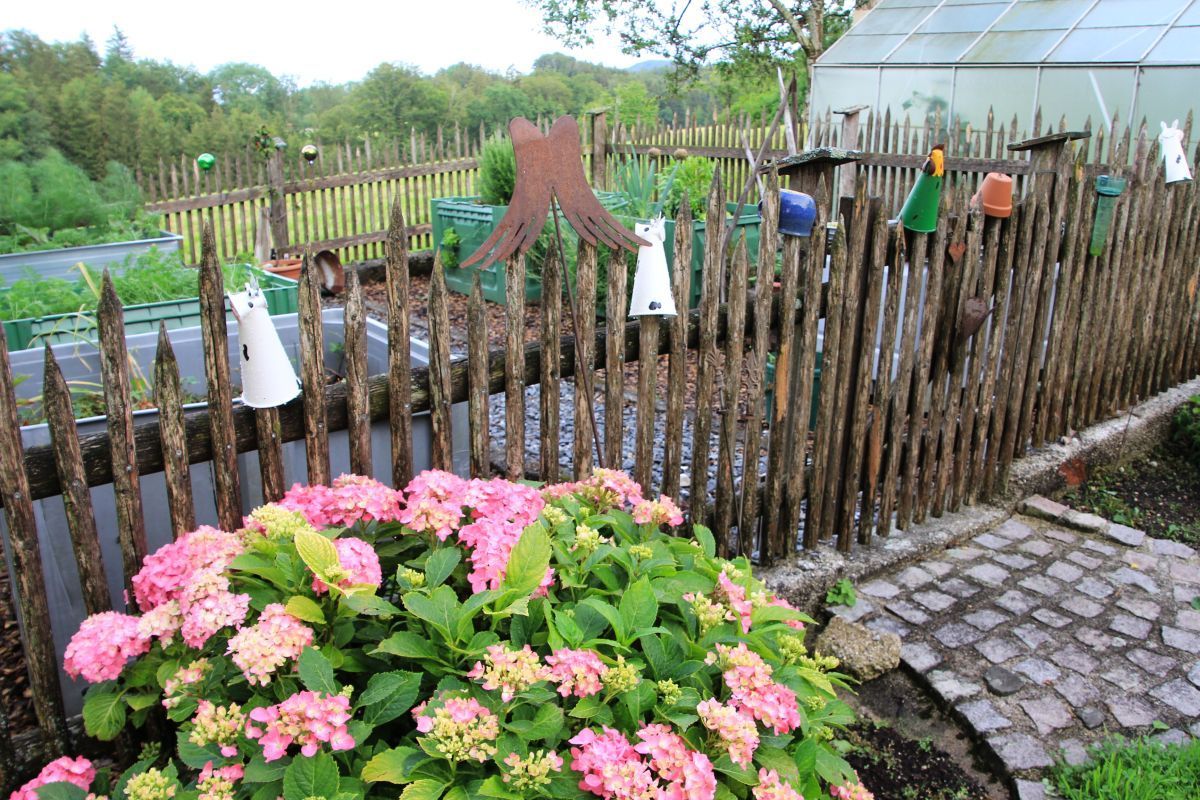 Una valla de madera con comederos para pájaros y un macizo de flores rosadas.