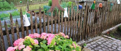 Una valla de madera con comederos para pájaros y un macizo de flores rosadas.