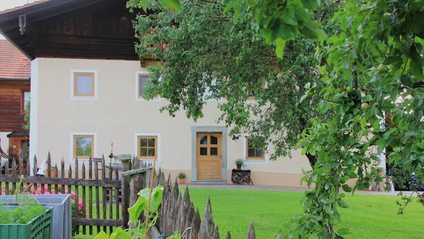 Un edificio a due piani con recinzione in legno, prato curato e un piccolo giardino con piante.