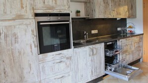 Una cucina con mobili bianchi in legno, forno a incasso, lavastoviglie e lavello in acciaio inossidabile.