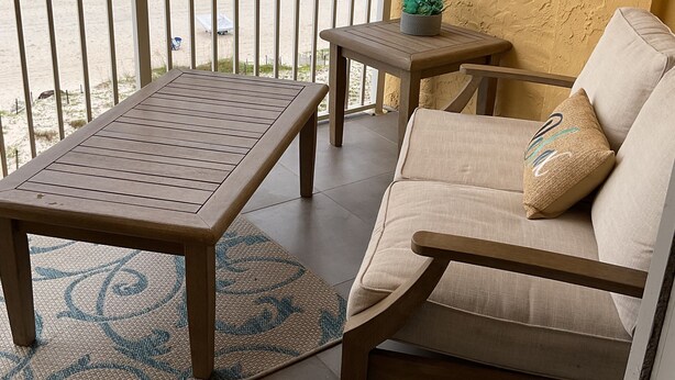 A balcony with a wooden table and sofa, a small table with a plant, and a view of the beach. - NEWLY RENOVATED-BEACH FRONT-TOP FLOOR-BRIGHT LIGHT-QUIET BUILDING (Gulf Shores)