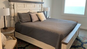 A neatly made bed with a headboard, two bedside lamps, and a view of the sea through a window. - NEWLY RENOVATED-BEACH FRONT-TOP FLOOR-BRIGHT LIGHT-QUIET BUILDING (Gulf Shores)