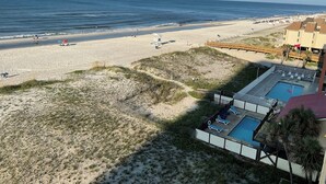 A beach view with a pool area, beach umbrellas, and a lifeguard stand. - NEWLY RENOVATED-BEACH FRONT-TOP FLOOR-BRIGHT LIGHT-QUIET BUILDING (Gulf Shores)
