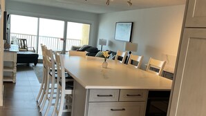 A modern kitchen with a central island, white cabinetry, and a dining area with chairs. - NEWLY RENOVATED-BEACH FRONT-TOP FLOOR-BRIGHT LIGHT-QUIET BUILDING (Gulf Shores)