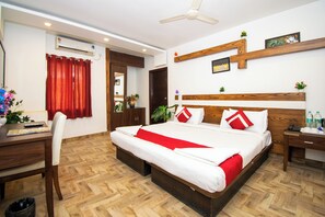 A hotel room with a large bed, wooden headboard, a desk with a chair, a small table with a phone and water bottles, and a ceiling fan. - Octave Verdisso Hotel (Bengaluru)