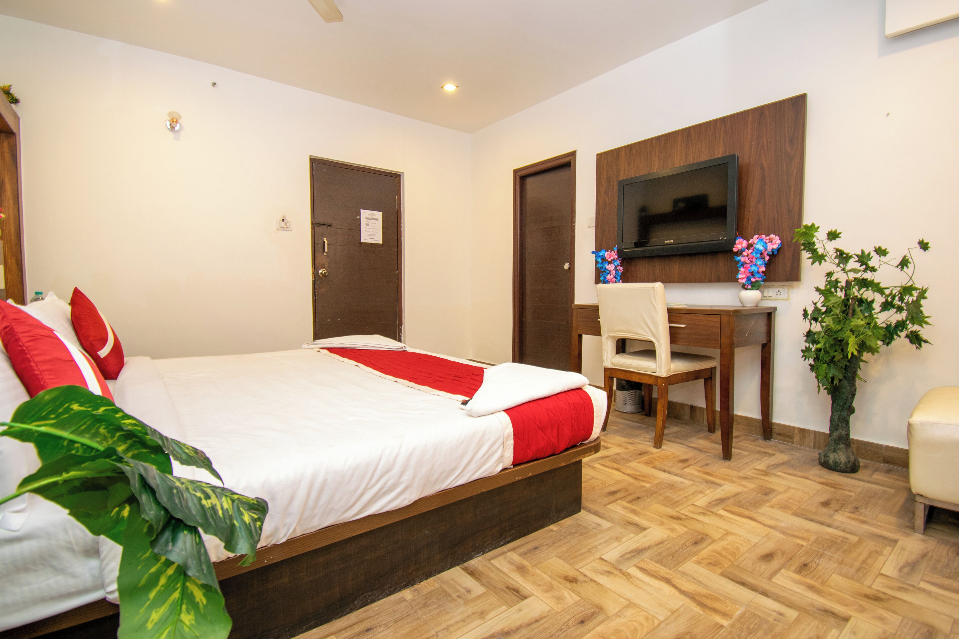A hotel room with a bed, a desk, a chair, a TV, and a potted plant.