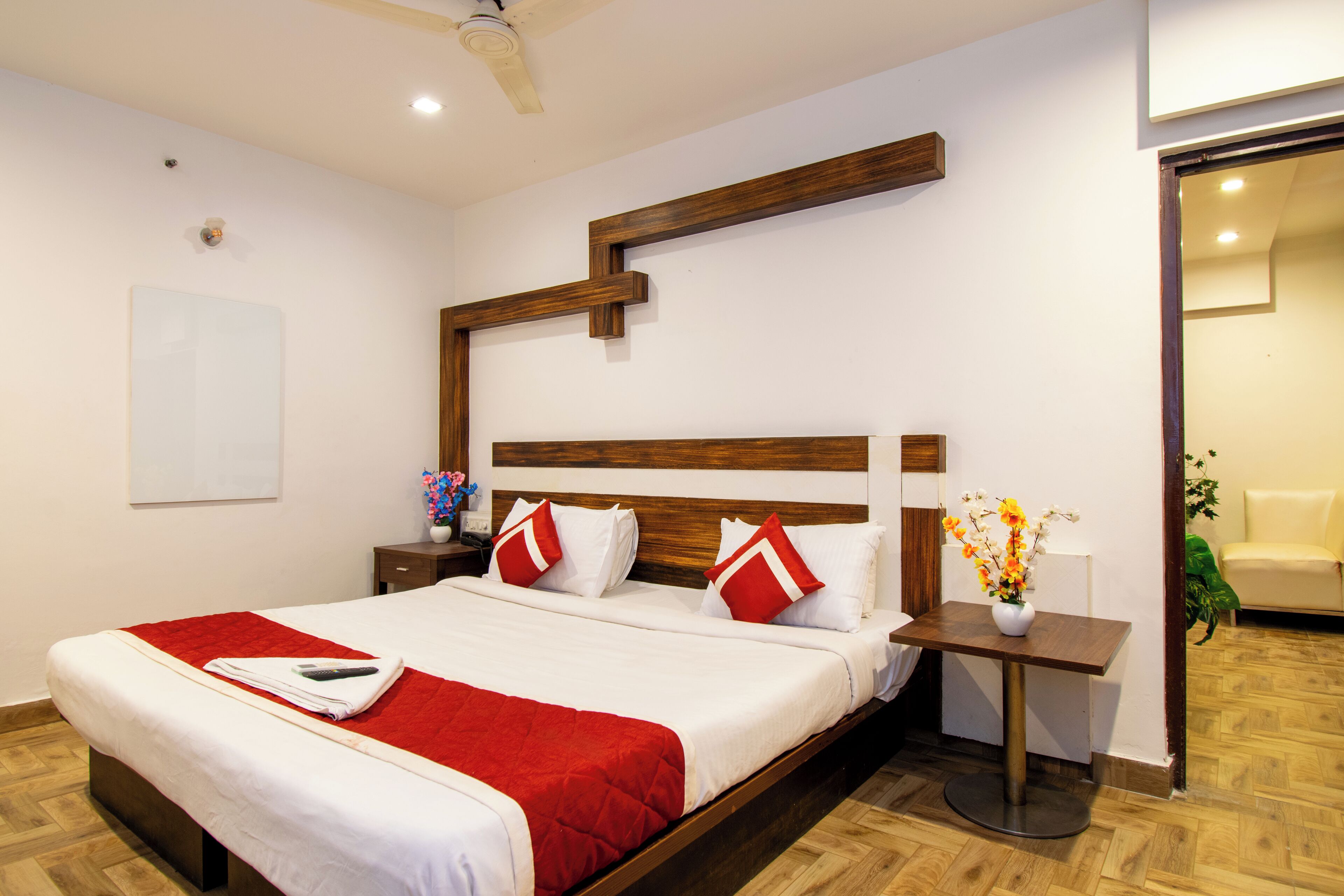 A hotel room with a large bed, wooden headboard, bedside tables, and a small table with a vase of flowers.