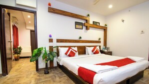 A hotel room with a wooden headboard, a large bed with white bedding and red accents, a bedside table with a lamp, and a potted plant. - Octave Verdisso Hotel (Bengaluru)