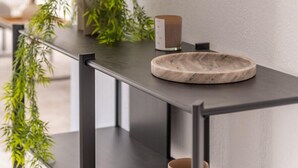 Et stilfuldt badeværelse med en marmorvask, et rundt spejl og en potteplante på et sort konsolbord.