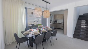 Un espace repas moderne avec une grande table dressée pour six personnes, entourée de chaises, et une cuisine en arrière-plan.