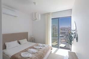 A hotel room with a bed, a window with curtains, a ceiling fan, and a view of the outside. - Protaras Semeli Villa Se8 (Paralimni)
