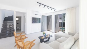 Un salon moderne avec un canapé, une table basse et des fauteuils. Un escalier mène à une autre pièce.