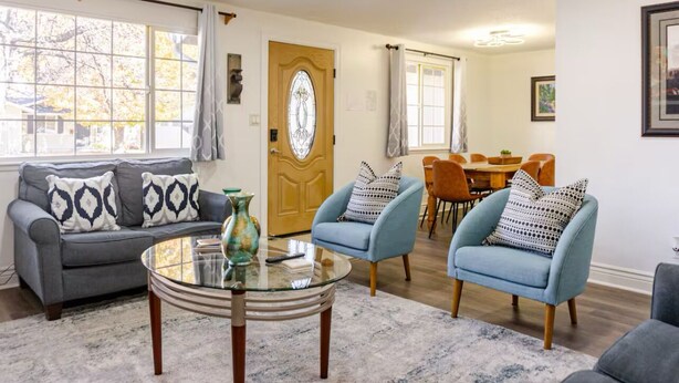 Un salon avec un canapé gris, deux fauteuils bleus, une table basse en verre et une porte en bois.