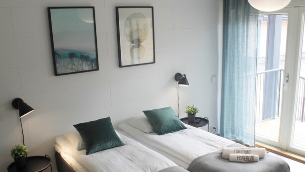 Ein modernes Hotelzimmer mit zwei Betten, einem kleinen Tisch, einer Lampe und Kunstwerken an der Wand.