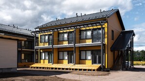 Ein modernes Gebäude mit zwei Etagen, einer gelben Fassade und einem schwarzen Dach.