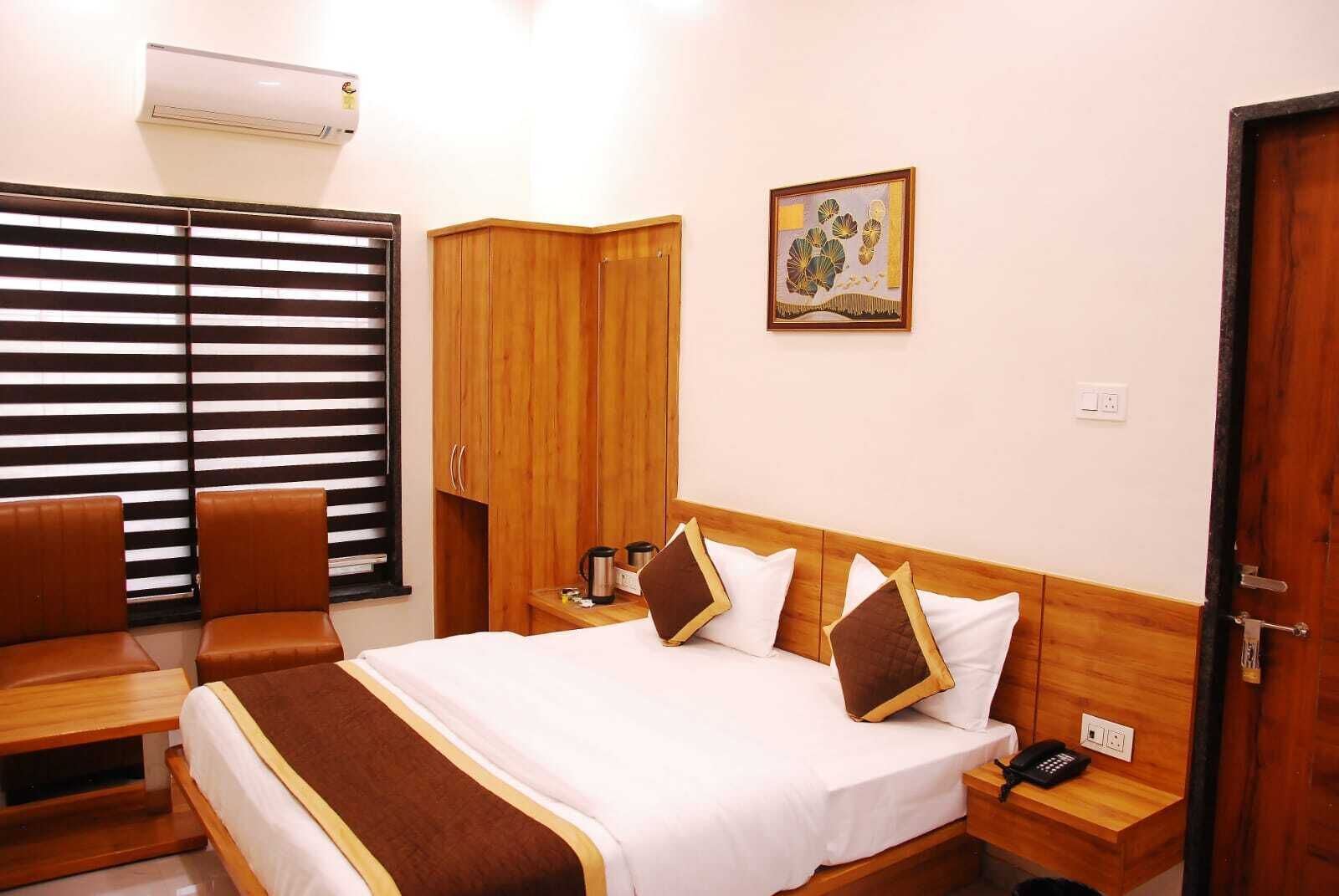A hotel room with a bed, a desk, a chair, a wardrobe, and a window with blinds.