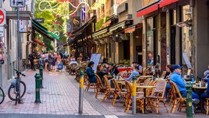 Uma rua com cafés ao ar livre, cadeiras de vime e mesas.