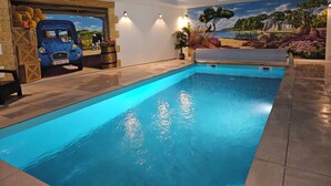 Une piscine intérieure dont le mur est décoré d’une fresque représentant une voiture bleue et un paysage de plage.