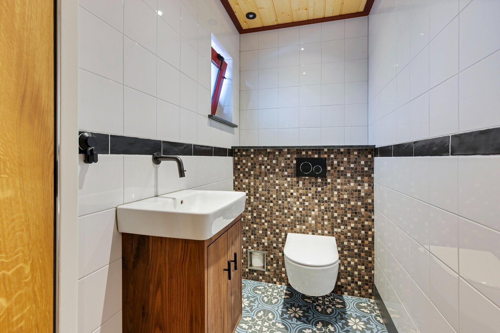 A bathroom with a white sink, wooden cabinet, tiled walls, and a mosaic-patterned shower area.