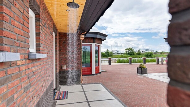 A brick building with a water feature, a red door, and a paved area with a planter.