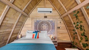 A bedroom with a sloped ceiling, a bed with blue bedding, a decorative wall tapestry, and an air conditioning unit.