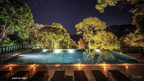 A pool at night surrounded by trees and a night sky.